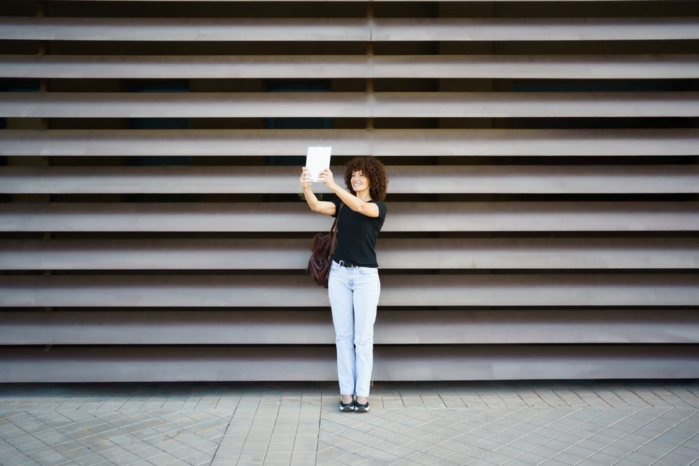 A Cheerful Woman Taking a Fun Selfie Against a Modern Textured Wall with a Big Smile