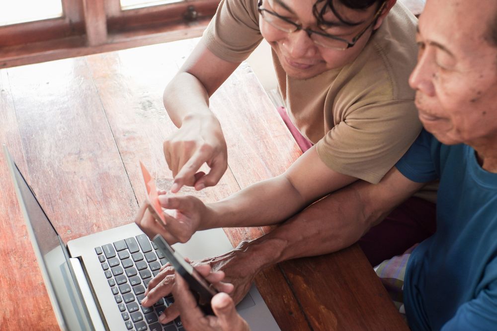 Happy adult son and older father pay online using laptop and credit card