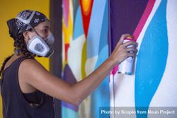 Side view of woman with bandana and gas mask creating a mural graffiti on wall 41OyZ0