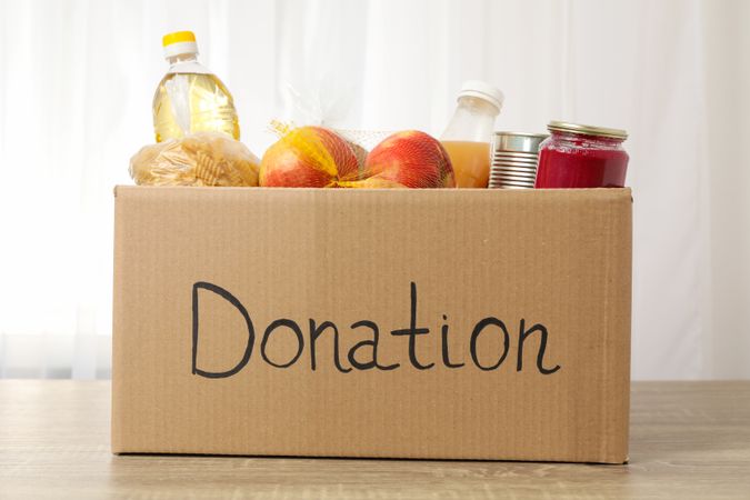 Donation box with different food on wooden table. Volunteering