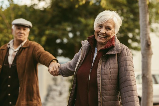 Smiling older woman holding hand of her partner and walking outdoors