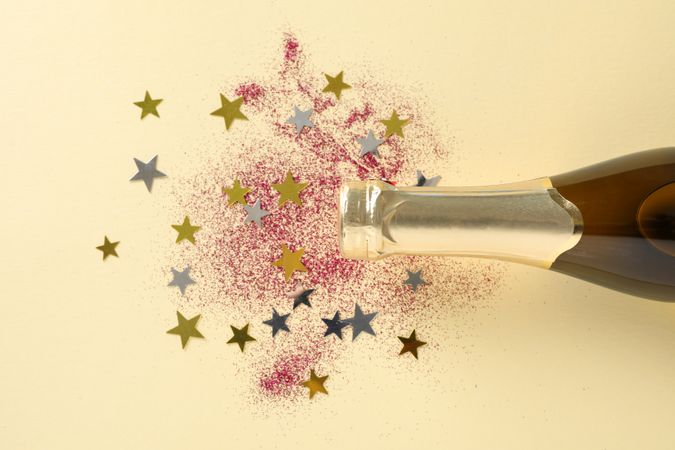 Champagne bottle and glitter on beige background, space for text