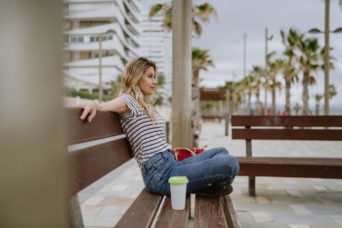 Happy woman with disposable cup of coffee sitting on street bench