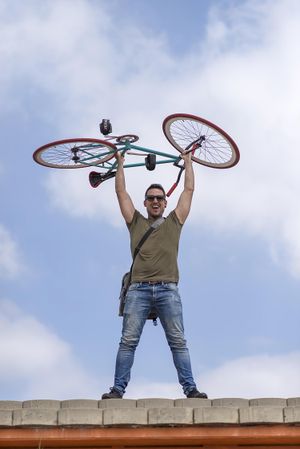 Happy male holding up bike with blue sky and clouds in background