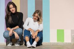 Happy girlfriends sitting against painted urban wall