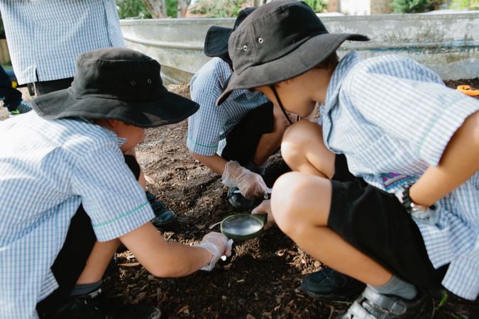 Kids holding a magnifying glass and looking at soil in the ground on a school field trip