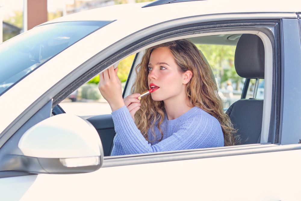 Young woman applying red lipstick in modern car on parking