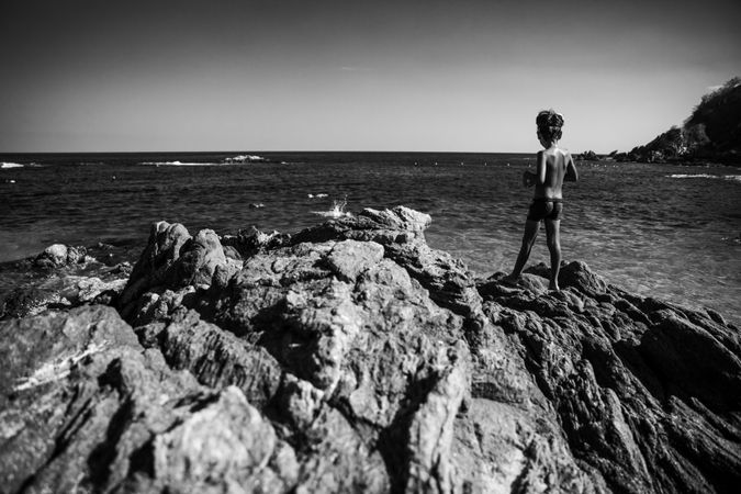 Little swimmer looking out at ocean from rocks