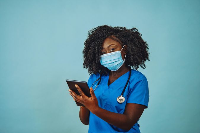 Portrait of Black medical professional in face mask dressed in scrubs holding tablet