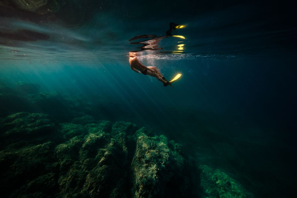 Unrecognizable man in flippers diving in blue ocean