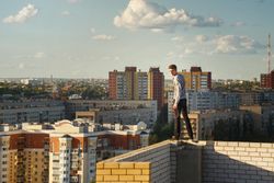 Male balancing on wall high above city