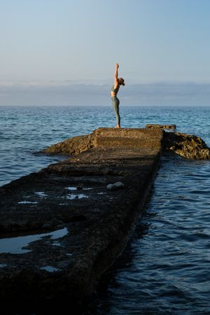 Slim woman doing yoga on stone pier