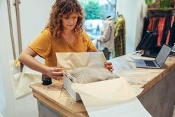 Woman preparing a package for delivery at clothing store checkout