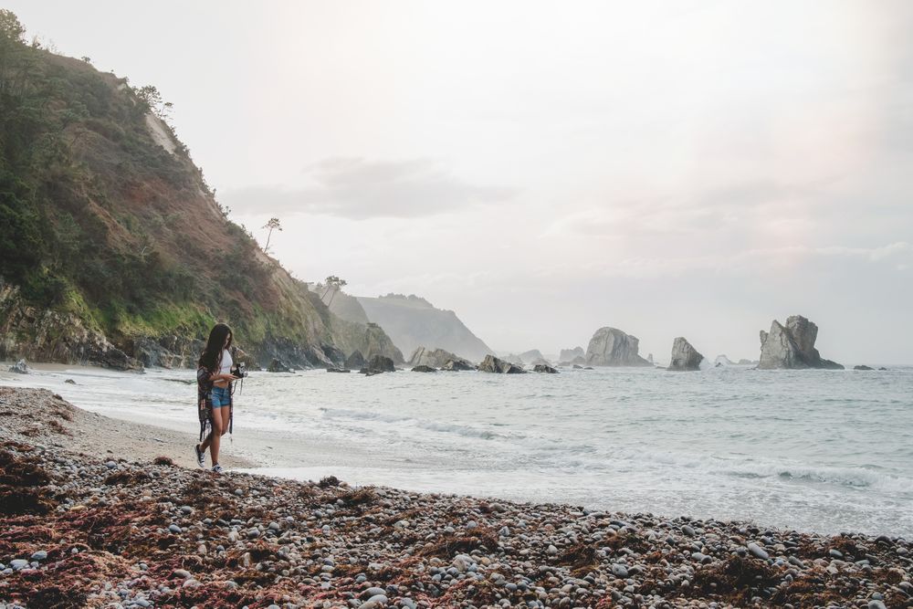 Woman with camera on shore near stones and water