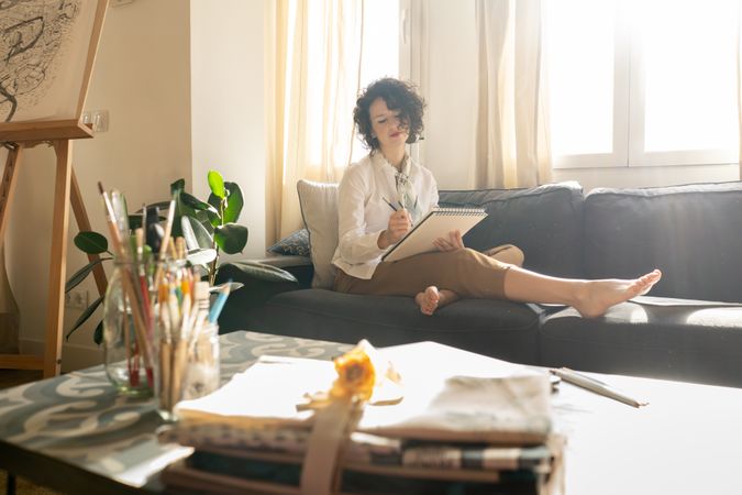 Woman writing on paper on sofa in room