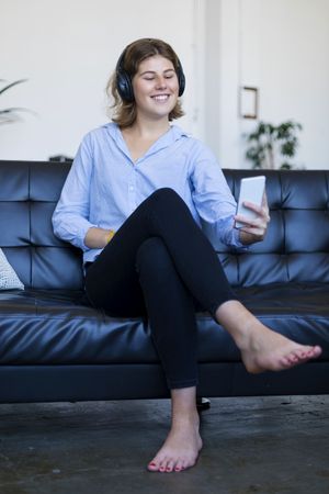 Barefoot brunette woman sitting on the sofa using mobile phone