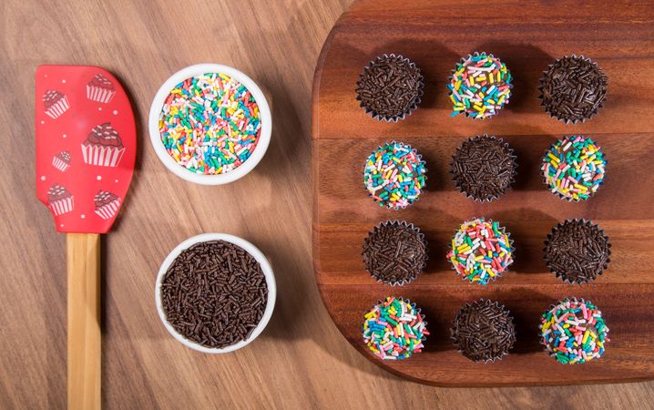 Top view of chocolate truffles with sprinkles presented on a wooden board with spatula