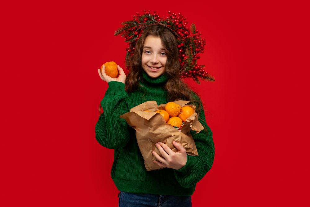 Young girl in green sweater holding paper bag of oranges