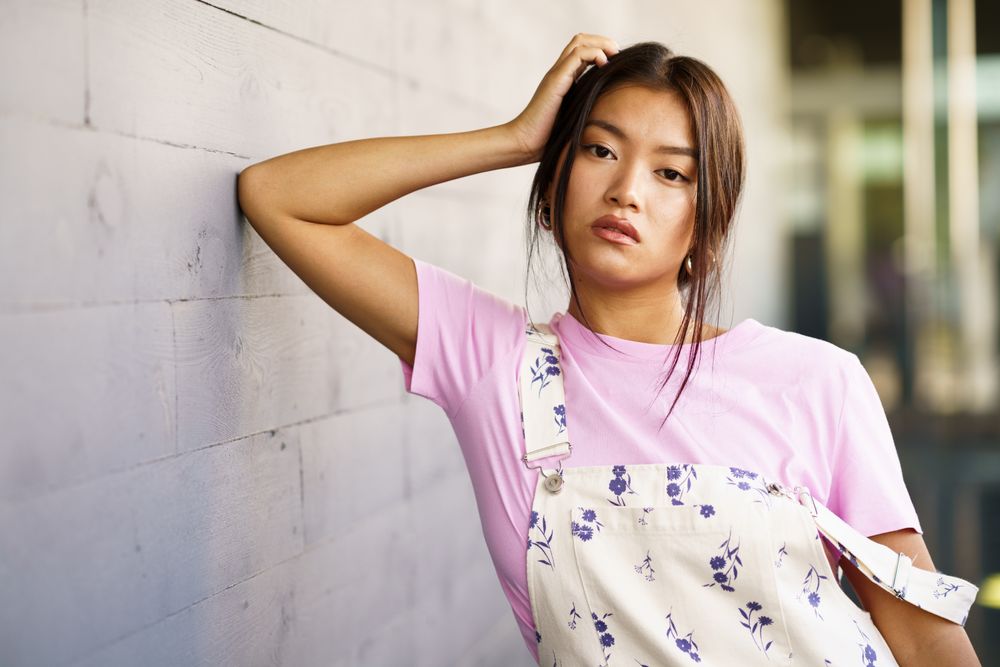 Serious female wearing casual clothes leaning against concrete wall, copy space