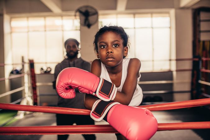 Confident looking girl in boxing gloves standing inside a boxing ring with her coach