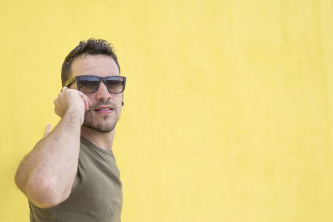 Calm male leaning on yellow wall talking on cell phone