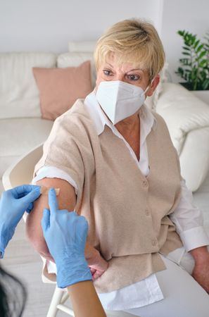 Crop doctor applying medical plaster on arm of mature woman
