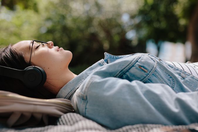 Side view of a woman relaxing outdoors listening to music wearing headphones