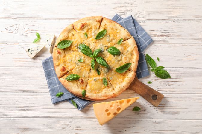 Towel, board, cheese pizza with basil on wooden background, copy space