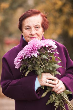 Portrait of older woman in purple coat holding bouquet of purple flowers