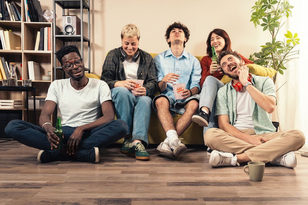 Diverse group of young friends laughing and watching a movie at home, eating popcorn.
