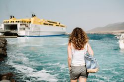 Curly woman looking at ship in water on seashore
