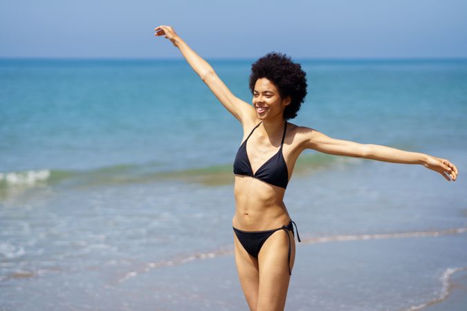 Happy woman walking on shore in bikini with outstretched arms