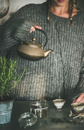 Blonde woman in cozy sweater pouring from traditional Japanese tea set