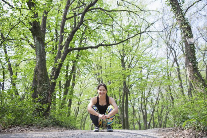 Smiling fit woman crouching down in forest before run
