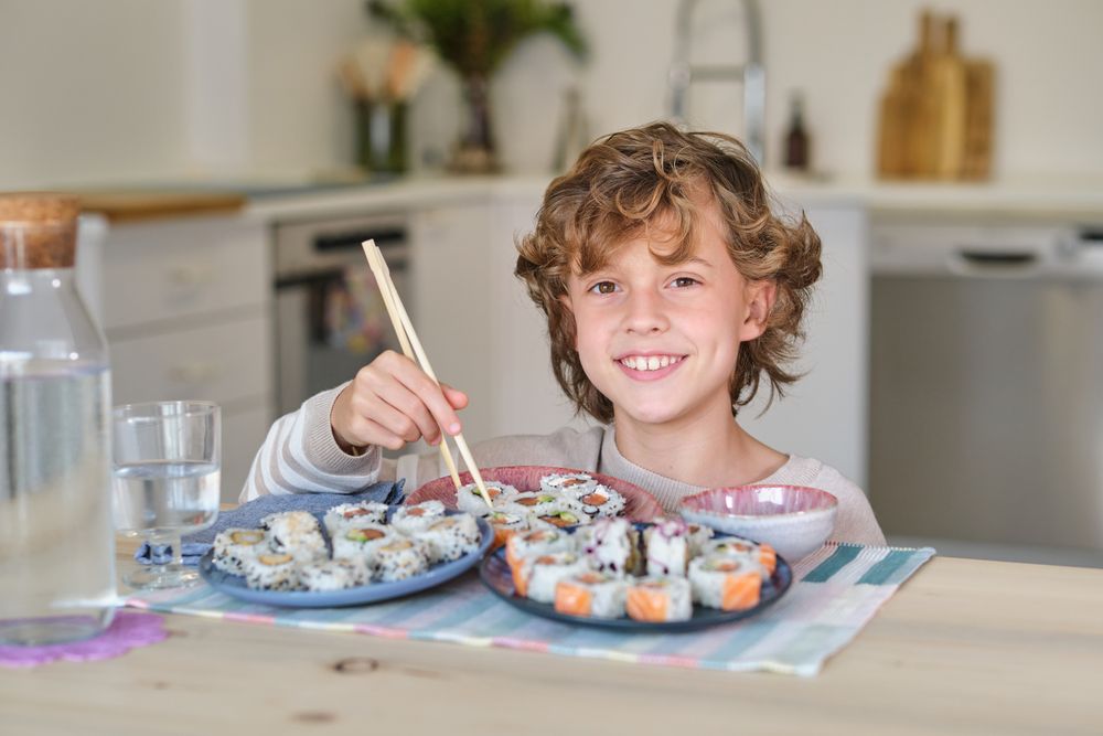 Boy enjoying sushi rolls in dining room at home