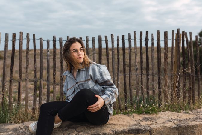 Trendy young female millennial resting on stone border at roadside