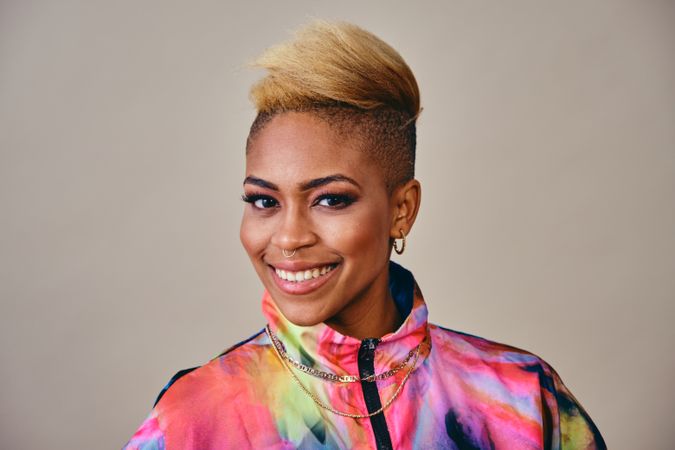 Studio shot of smiling Black woman in bold 80s windbreaker jacket and gold jewelry