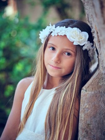 Cute girl in wreath sitting and looking at camera while leaning