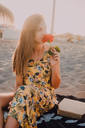 Woman sitting and sniffing rose at beach