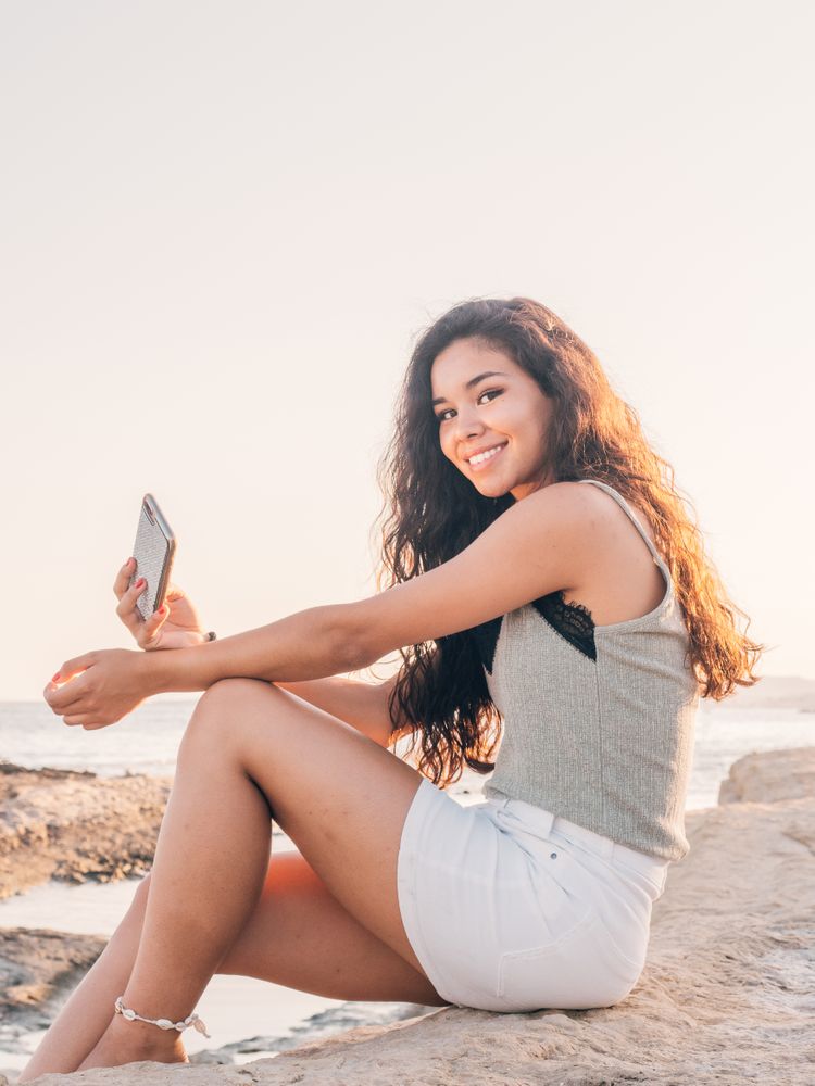 Dreamy trendy young woman texting on beach