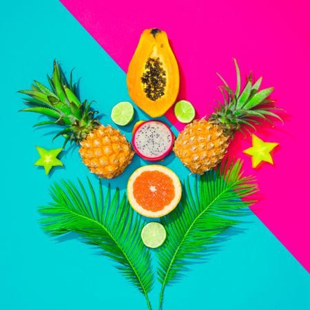 Tropical fruit, pineapple, papaya, dragonfruit on bright blue and pink background with palm leaves
