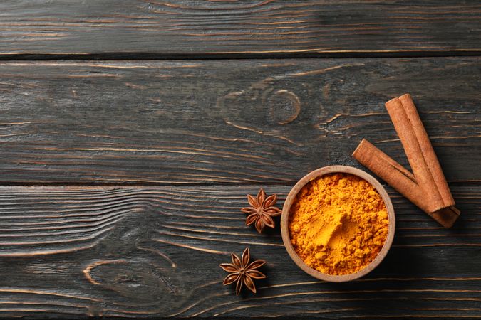 Bowl of turmeric with cinnamon sticks and anise, copy space