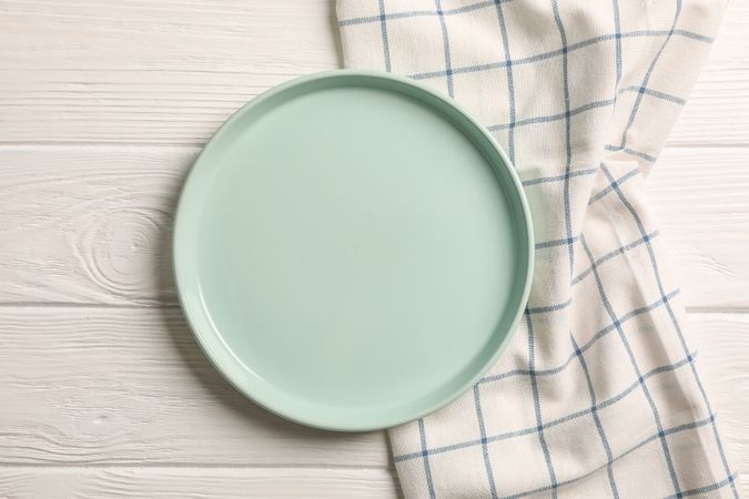 Kitchen towel with plate on wooden background, top view