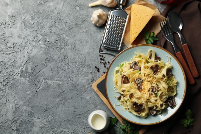 Composition with plate of tasty pasta and ingredients for cooking on gray background