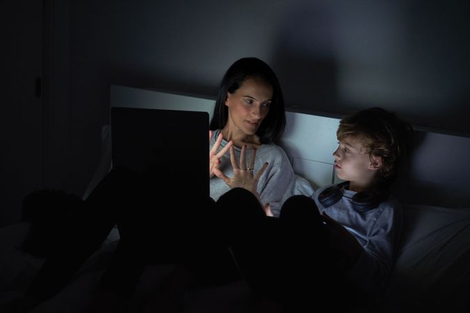 Woman and kid watching movie on laptop in bedroom at night