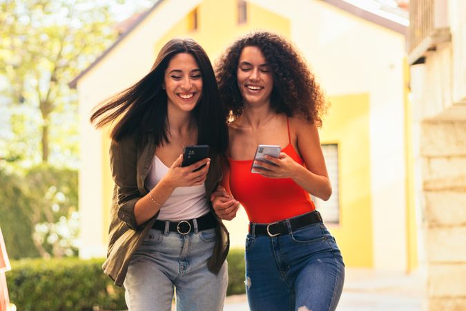 female couple laughing using mobiles going up stairs