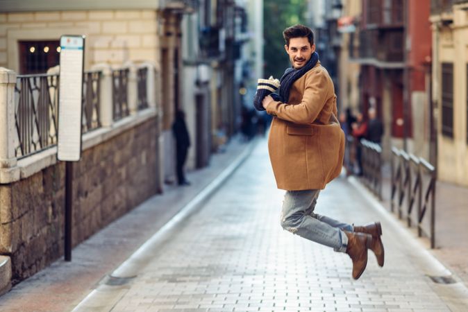 Happy man jumping in winter clothes in the street