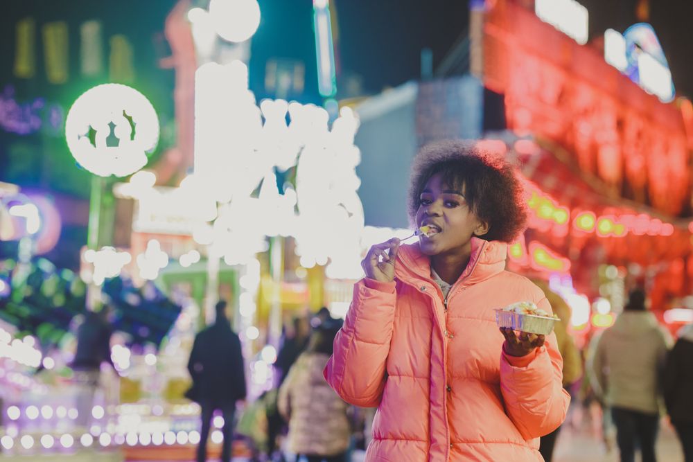 Black woman snacking in amusement park at night