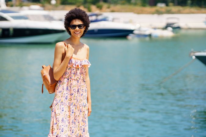 Happy female in maxi dress standing on dock on sunny day