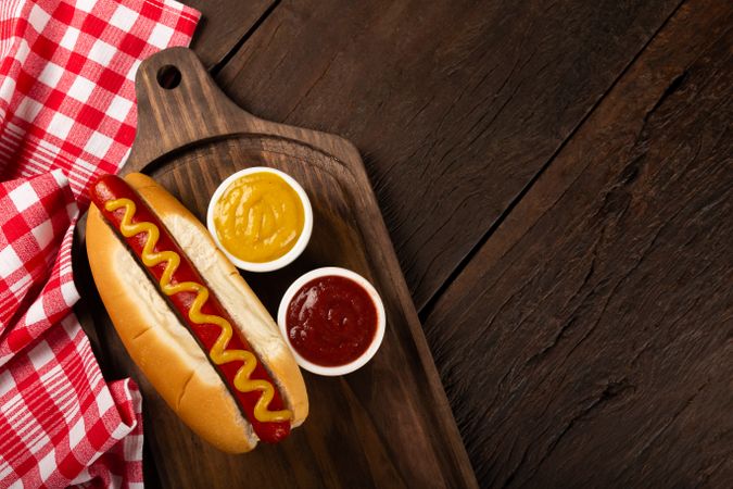 Top view of hot dog with mustard on wooden board and space for text